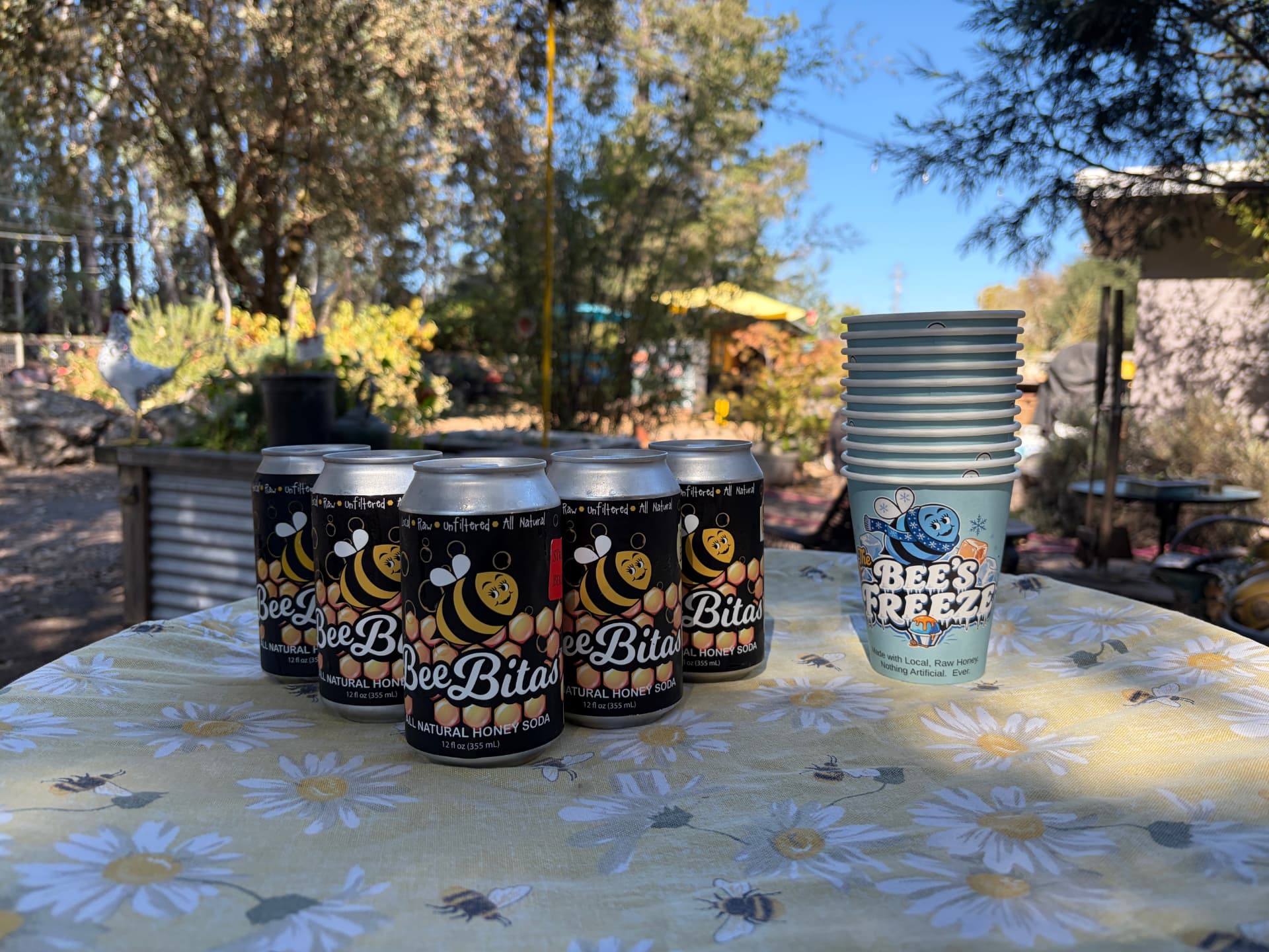 BeeBitas cans and a Bee's Freeze cup on a daisy tablecloth on the farm
